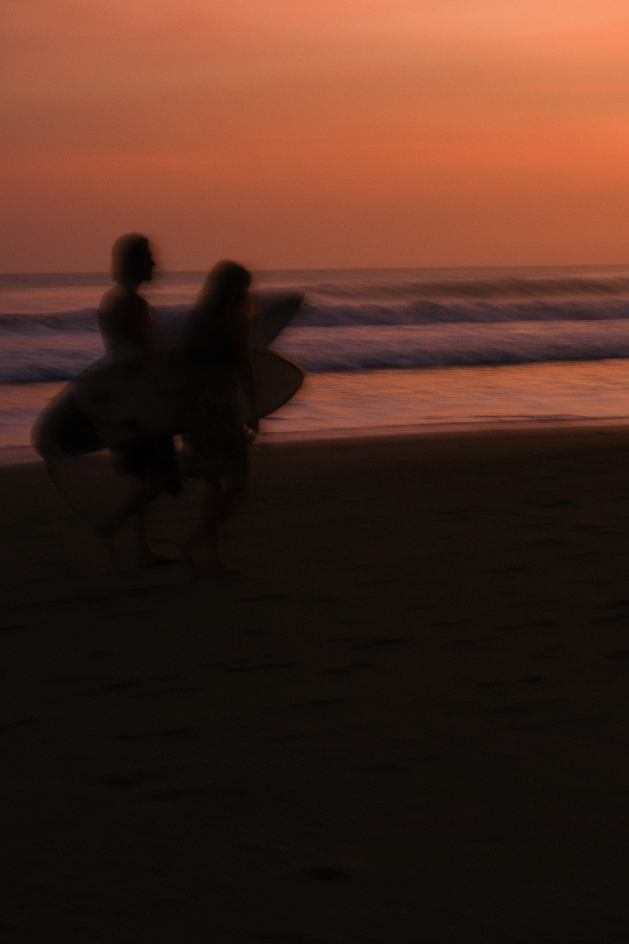 Surfers crossing the beach in the orange light of sunset