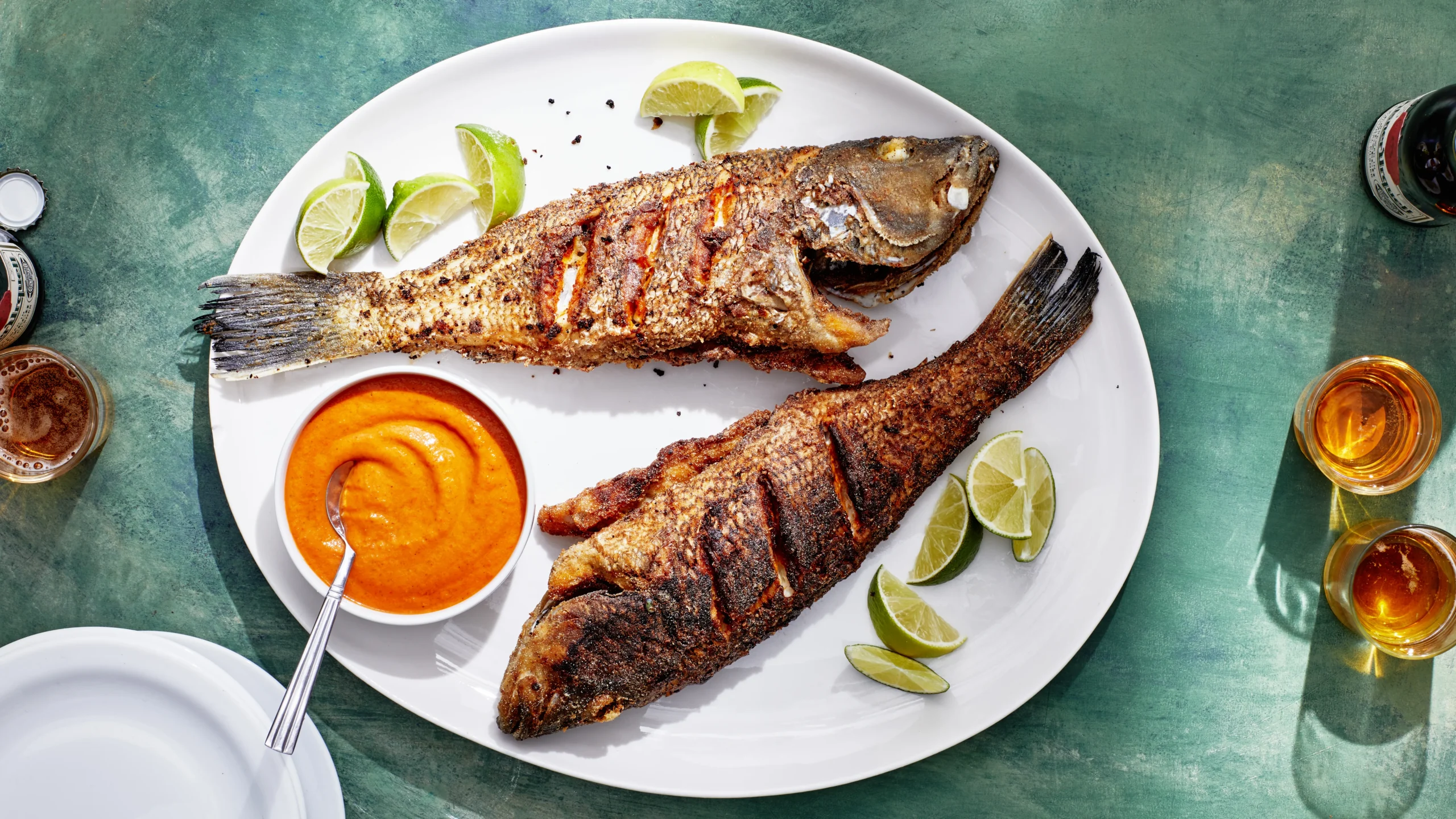 Two fried fish served with lime wedges and orange sauce